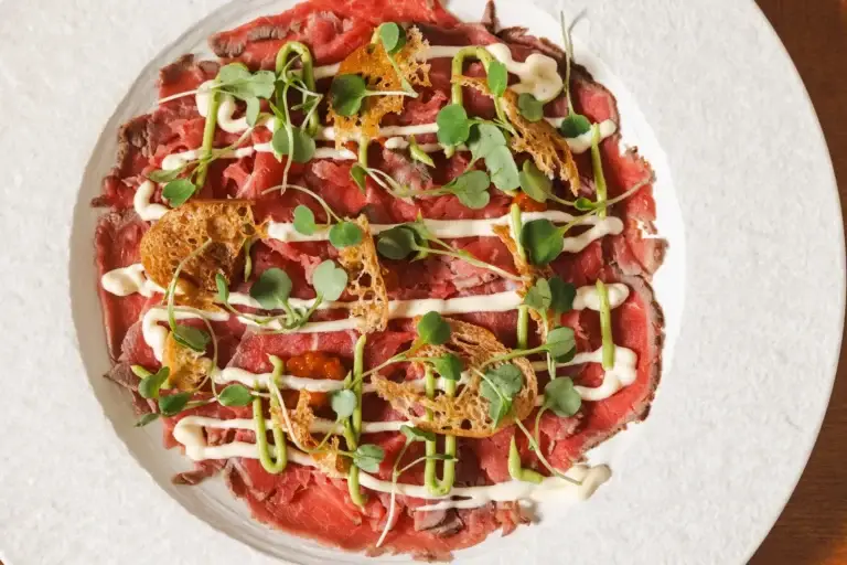 Beef Carpaccio with microgreens, a creamy drizzle and crispy croutons, seen from above at Capriciano Osteria