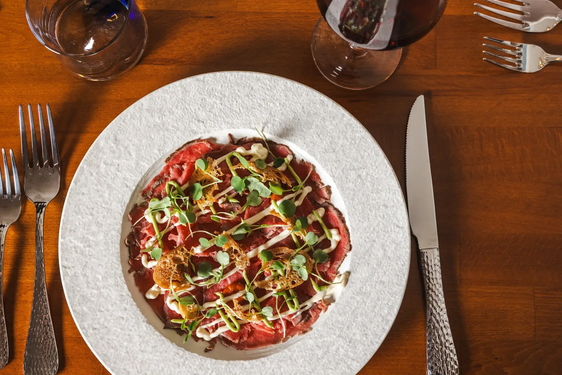 Beef Carpaccio with microgreens and a crispy topping beside a glass of red wine at Capriciano Osteria