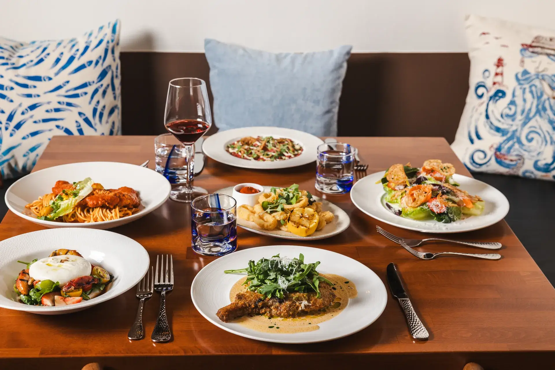 Booth table with six shared plates, including calamari and burrata, with red wine at Capriciano Osteria