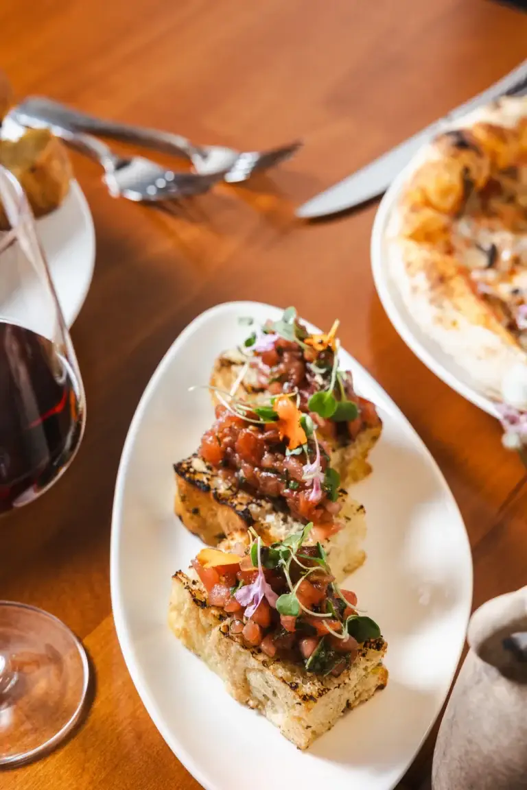 Bruschetta al Pomodoro on an oval plate beside a glass of red wine at Capriciano Osteria