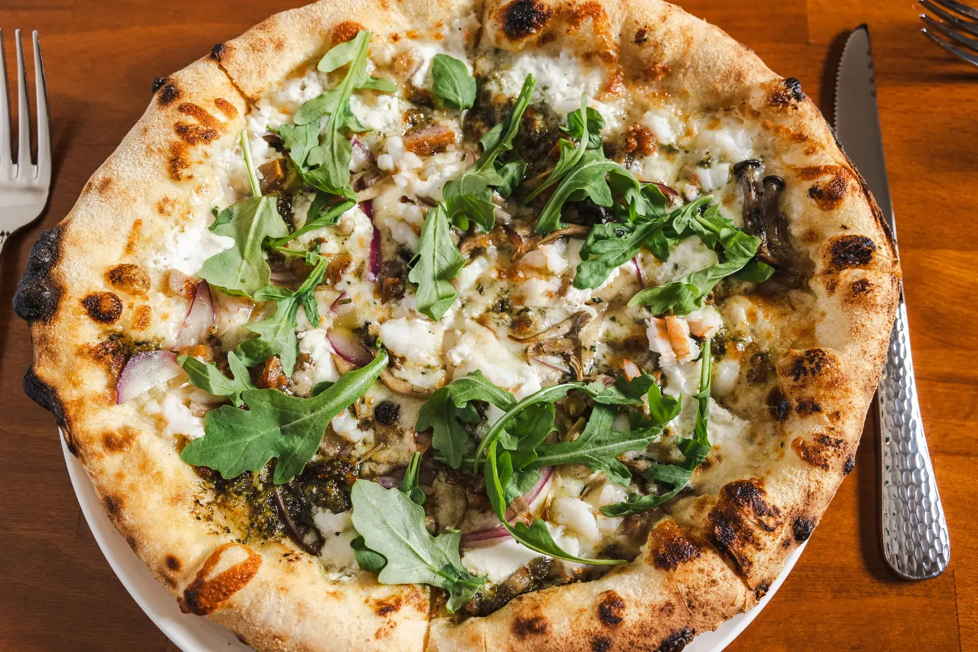 Close-up of a white pizza with ricotta, pesto, red onion and arugula at Capriciano Osteria