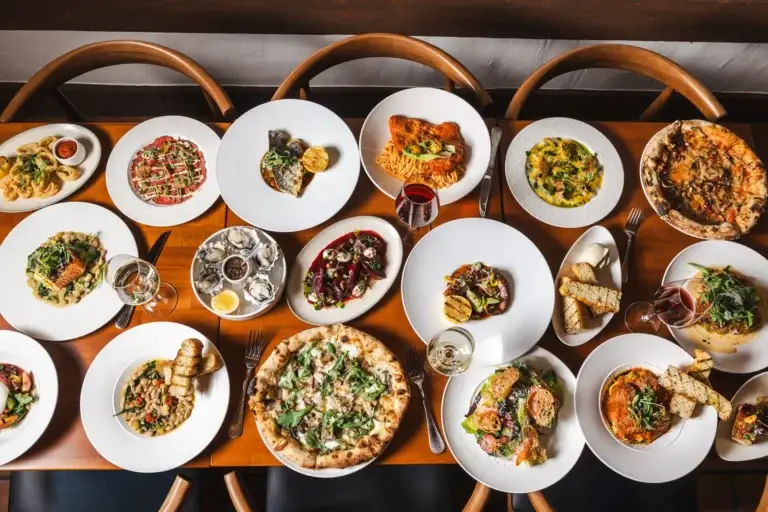 A long table covered with shared pizzas, oysters and octopus for a group dinner at Capriciano Osteria