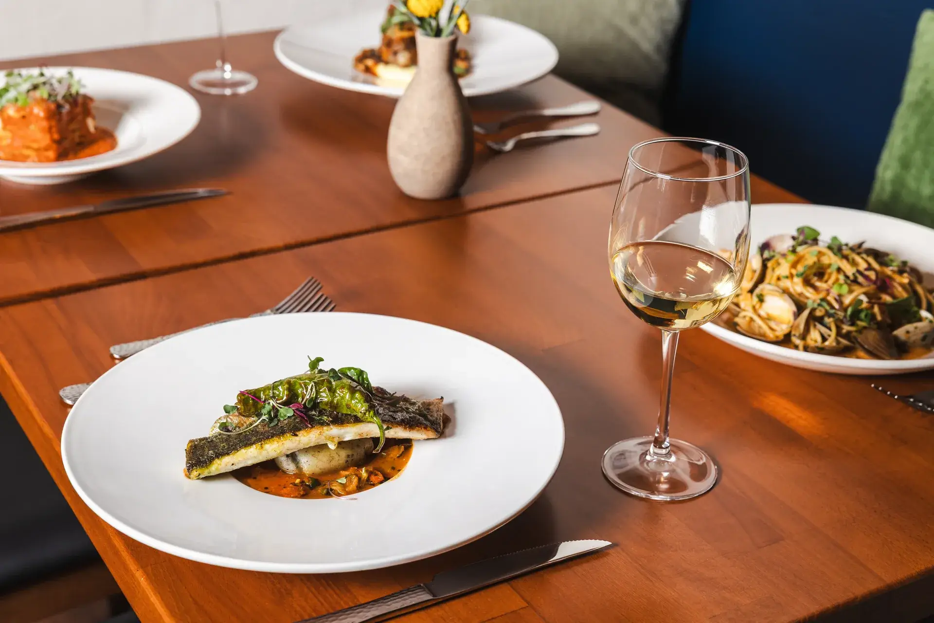 Joined tables with fish, clam pasta, lasagna and a creamy pasta, white wine and flowers at Capriciano Osteria
