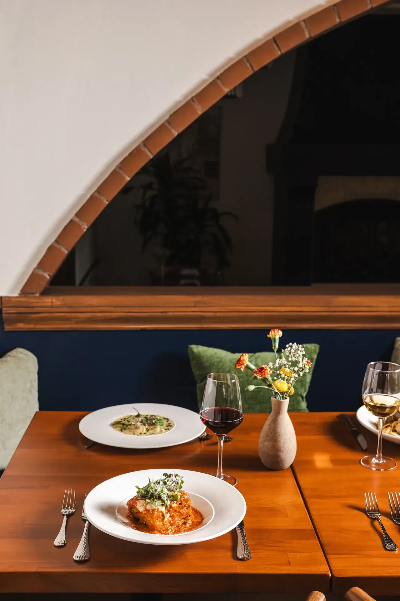 Lasagna and a creamy pasta with red and white wine under a brick-edged arch at Capriciano Osteria