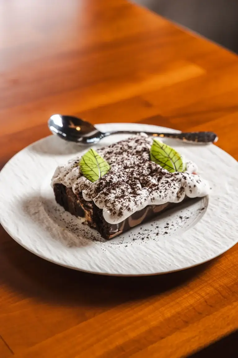 Layered cake with white cream, cocoa crumbs and green leaf decorations on a white plate at Capriciano Osteria