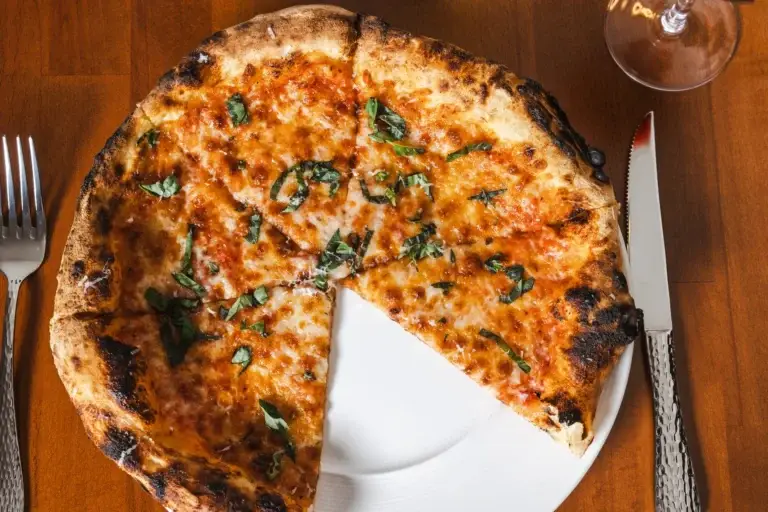 Firewood Oven Pizza 3 Margherita pizza with tomato and basil, one slice taken, on a wood table at Capriciano Osteria
