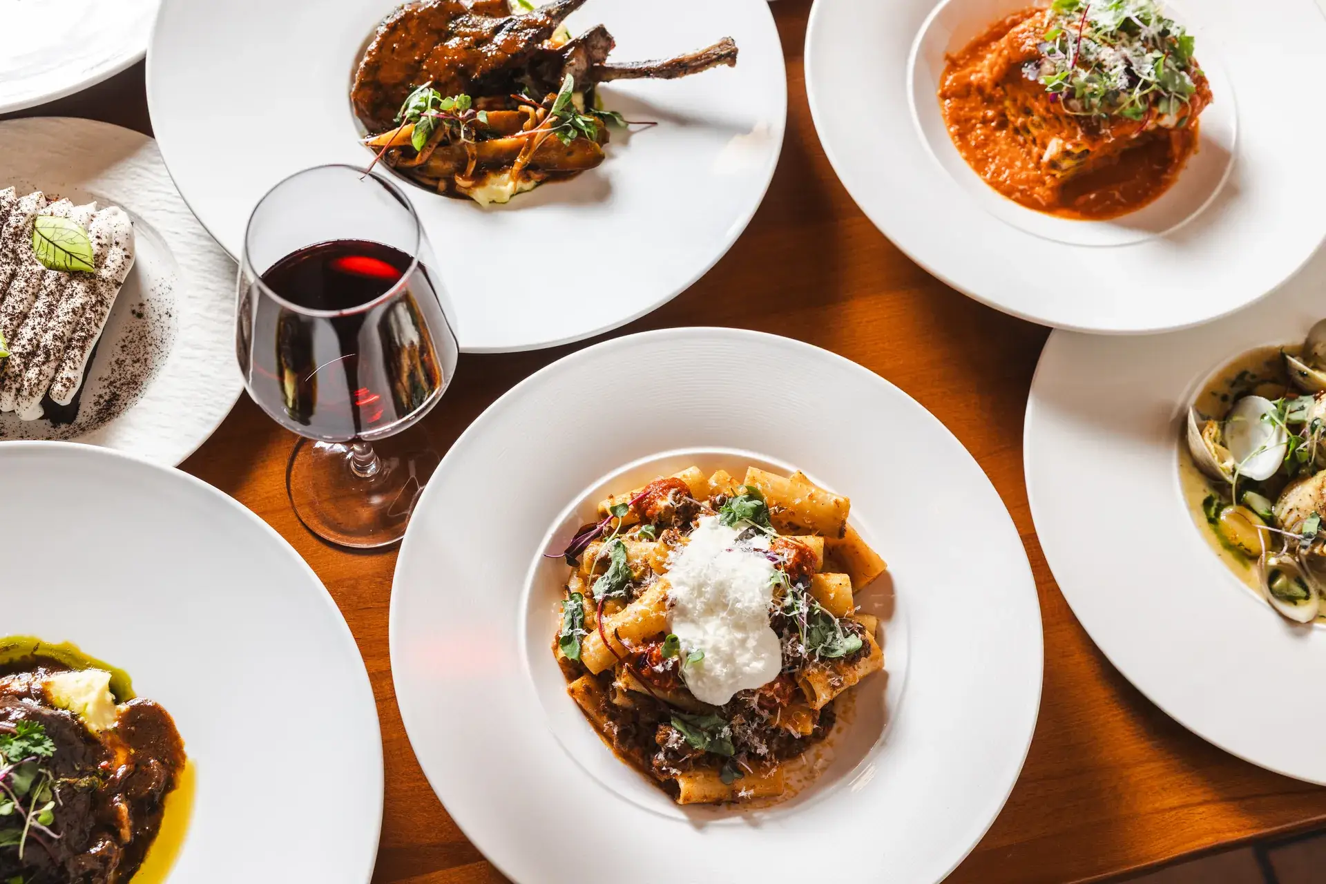 Overhead of rigatoni, lamb chops, lasagna, braised meat and dessert with red wine at Capriciano Osteria