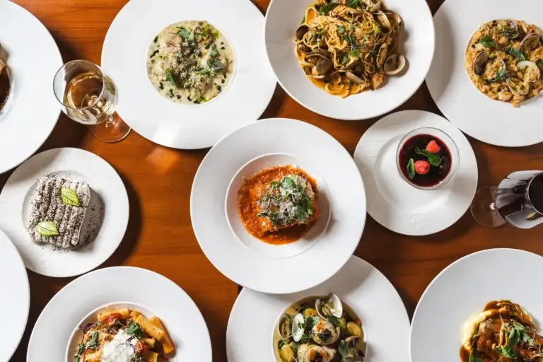 Overhead table of ravioli, clam spaghetti, risotto, lasagna, rigatoni and desserts at Capriciano Osteria