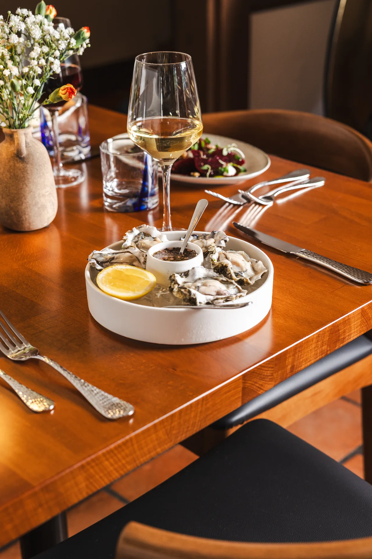 A Wine Pairing Guide for Italian Seafood 3 Oysters on the half shell with white wine, beet salad and flowers on a table at Capriciano Osteria