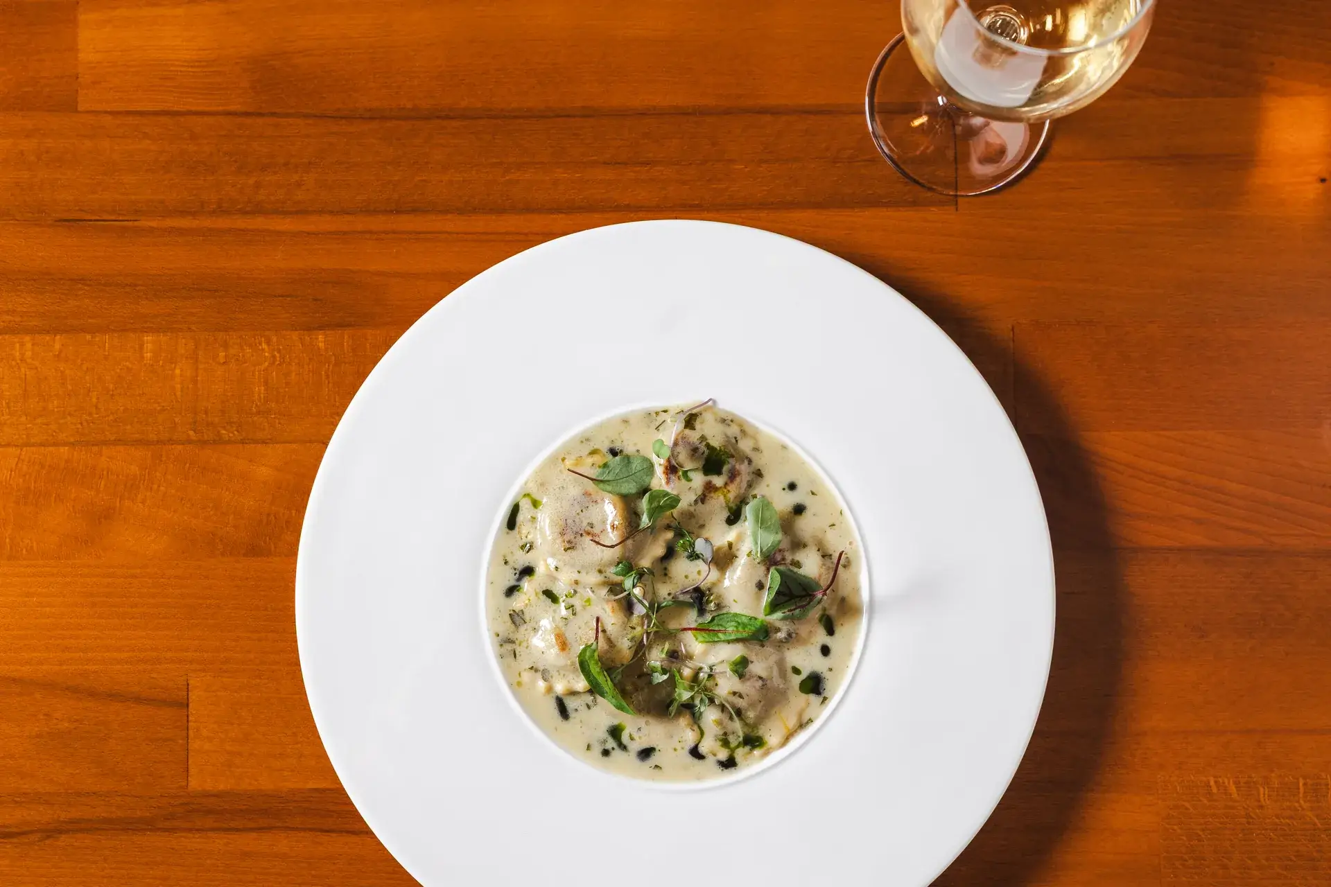 Ravioli in a cream sauce with herbs, seen from above on a wood table at Capriciano Osteria