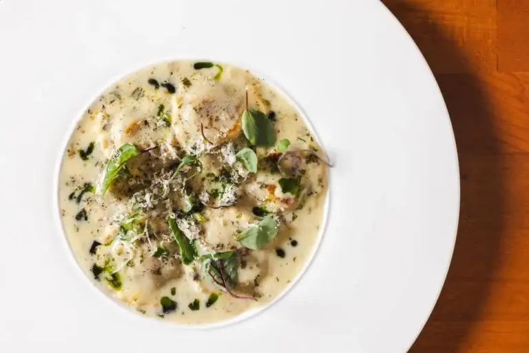 Ravioli in a pale cream sauce with herbs and green oil, seen from above at Capriciano Osteria