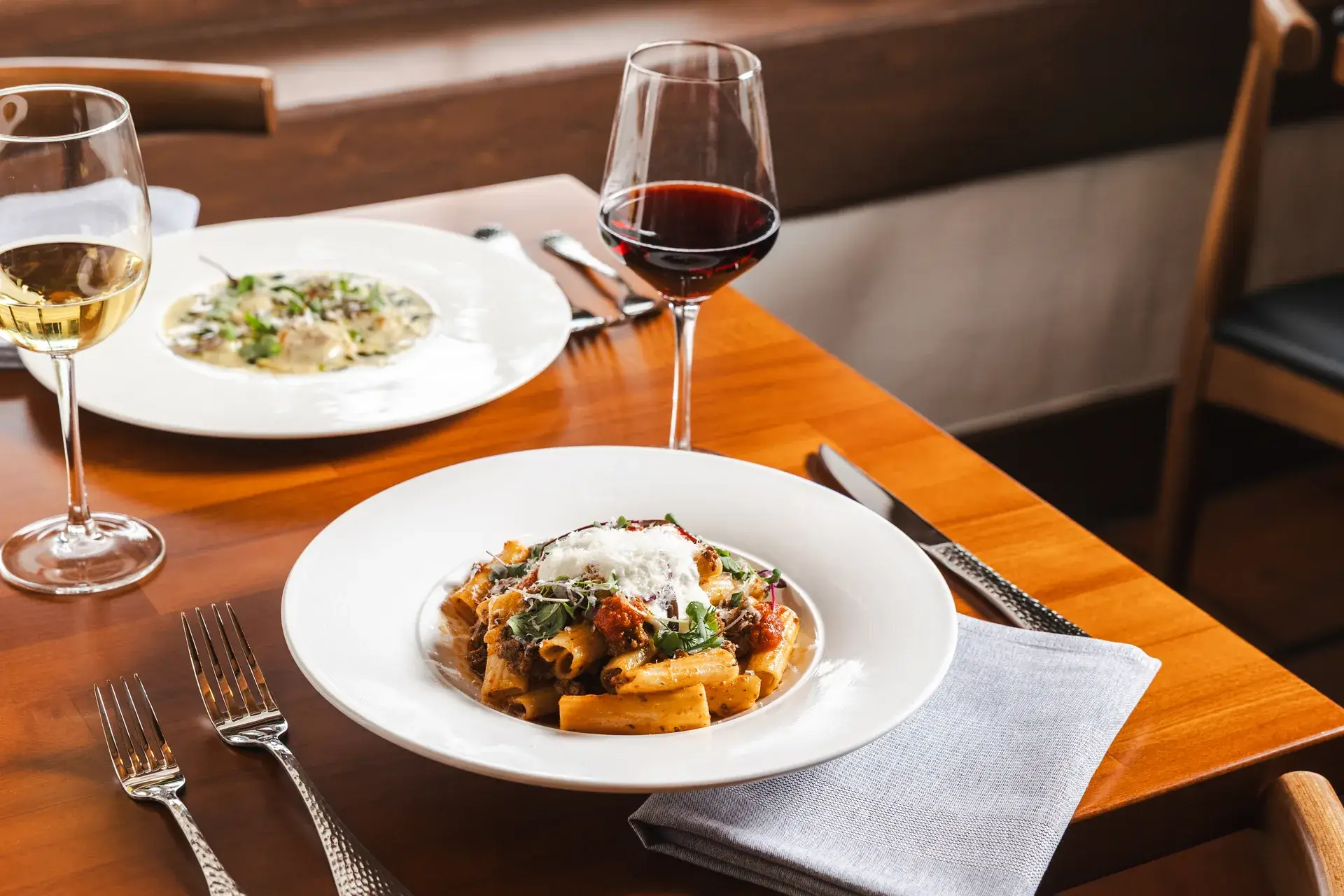 Rigatoni and creamy ravioli with glasses of red and white wine on a table for two at Capriciano Osteria