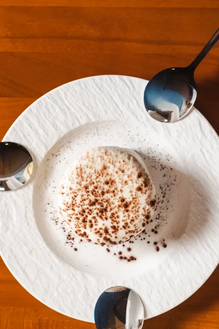 Blog 17 Round cream-topped dessert with a cocoa dusting and three spoons, seen from above, at Capriciano Osteria