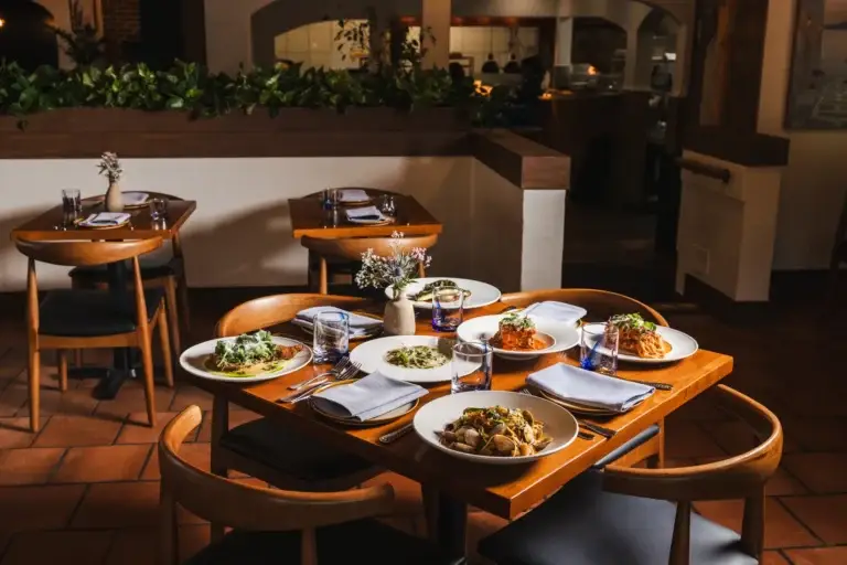 The dining room at Capriciano Osteria, a table for four set in front of the warm-lit open kitchen