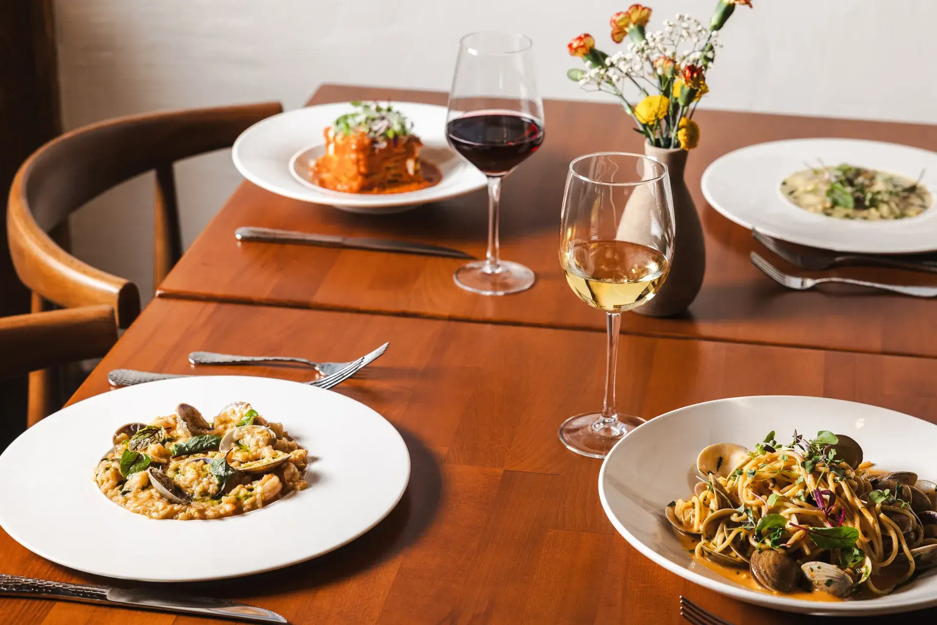 Shared plates of risotto, clam spaghetti, lasagna and pasta with wine and flowers at Capriciano Osteria