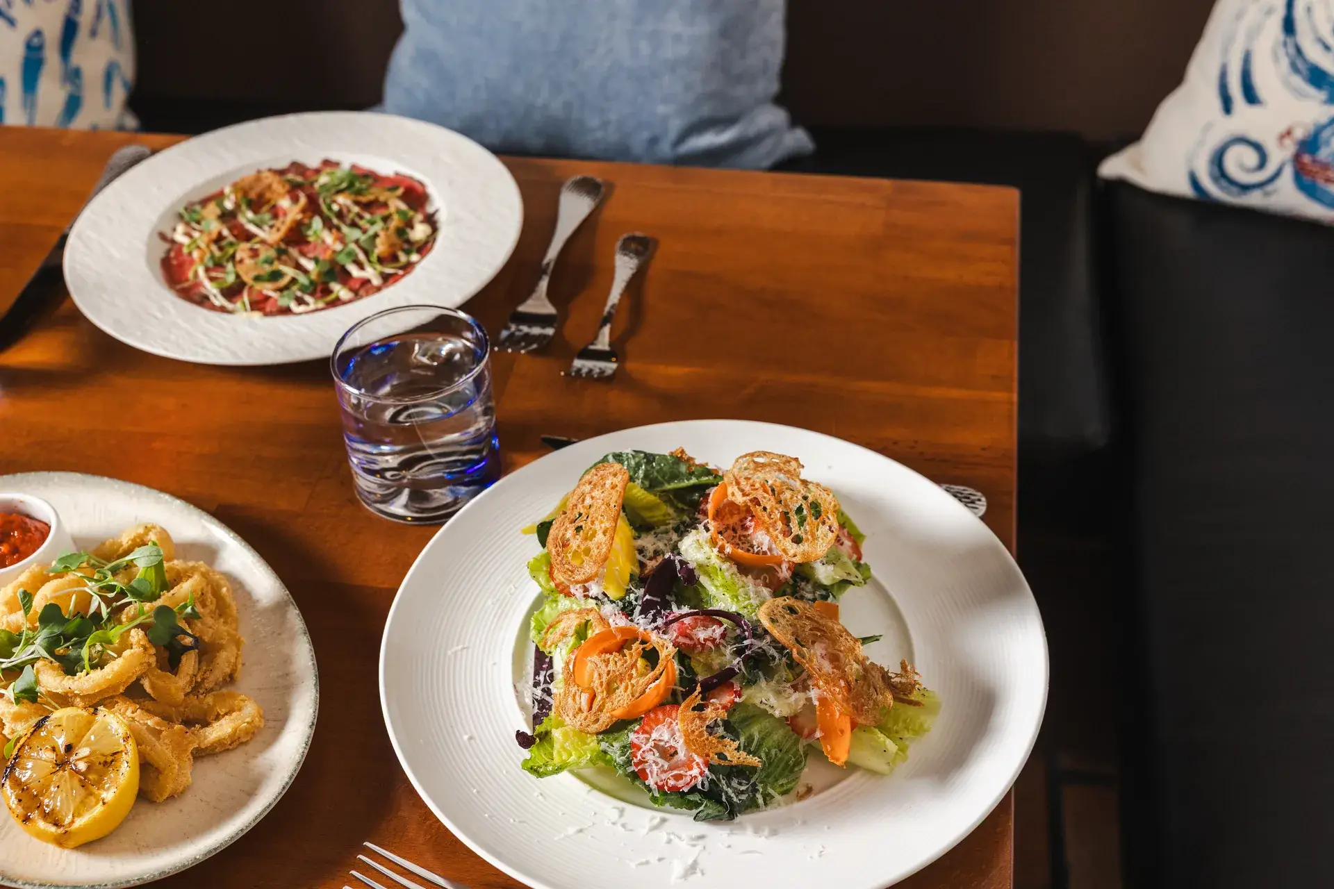 Small plates of fried calamari, salad with croutons and carpaccio on a table at Capriciano Osteria