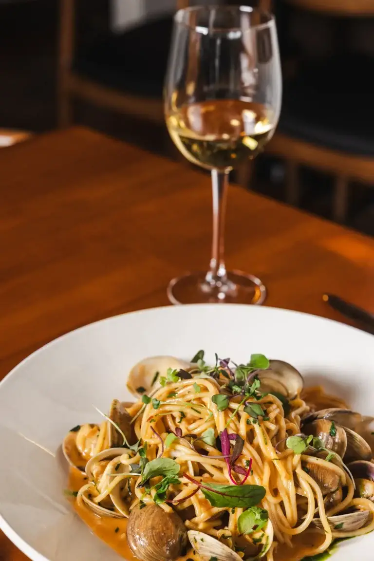 Spaghetti con Gamberi e Vongole with clams and shrimp beside a glass of white wine at Capriciano Osteria