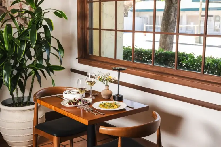 Make a Reservation 5 Table for two by a large window with a potted plant and flowers at Capriciano Osteria