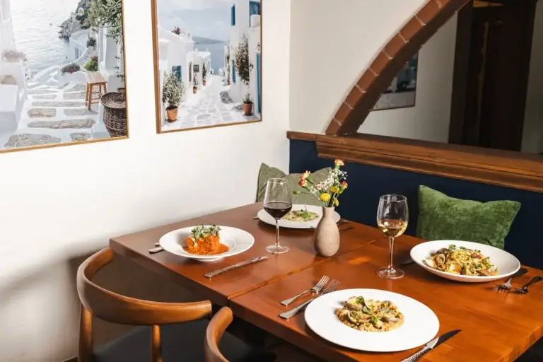 Make a Reservation 4 Two set tables beside framed Mediterranean coast prints under an arch at Capriciano Osteria