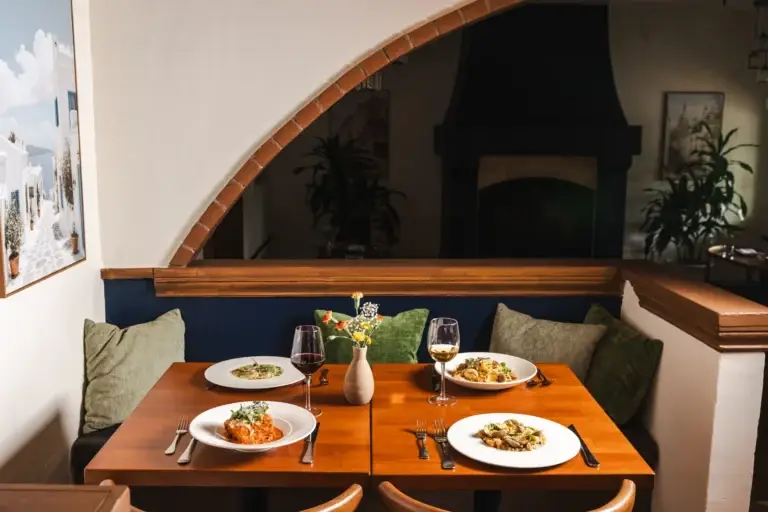 Contact 3 Two tables with green cushions under a brick-edged arch, the fireplace beyond, at Capriciano Osteria