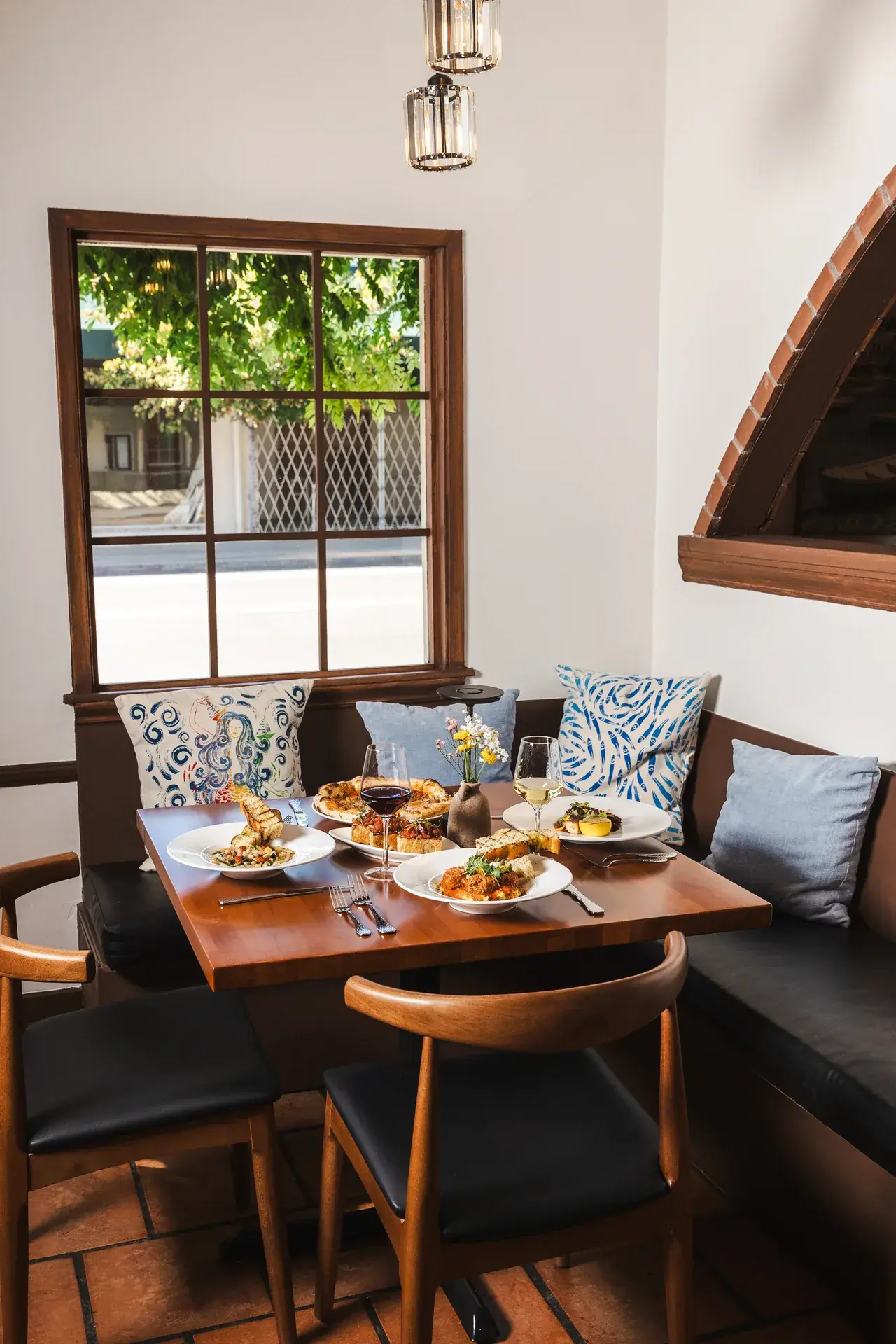 Osteria vs Trattoria vs Ristorante: What's the Difference? 2 Window booth with patterned pillows, wooden chairs and a terracotta floor at Capriciano Osteria