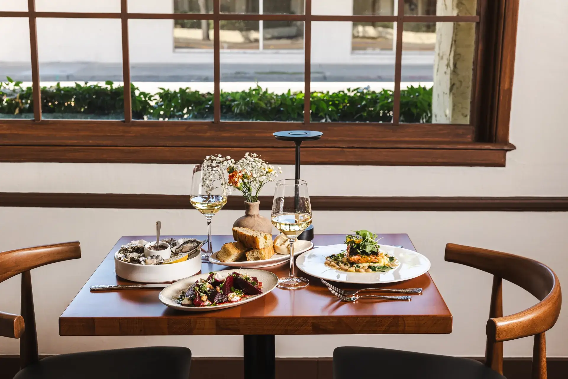 Window table for two set with small plates, wine and flowers at Capriciano Osteria