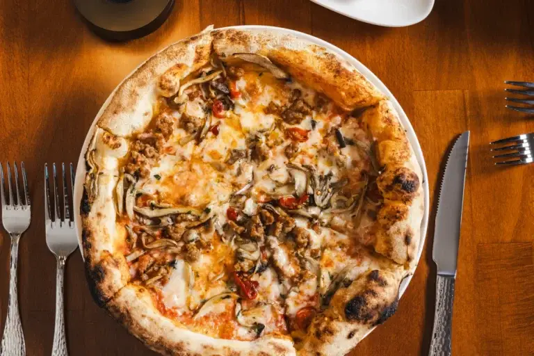 Wood-fired pizza with mushrooms, sausage and melted cheese, seen from above at Capriciano Osteria